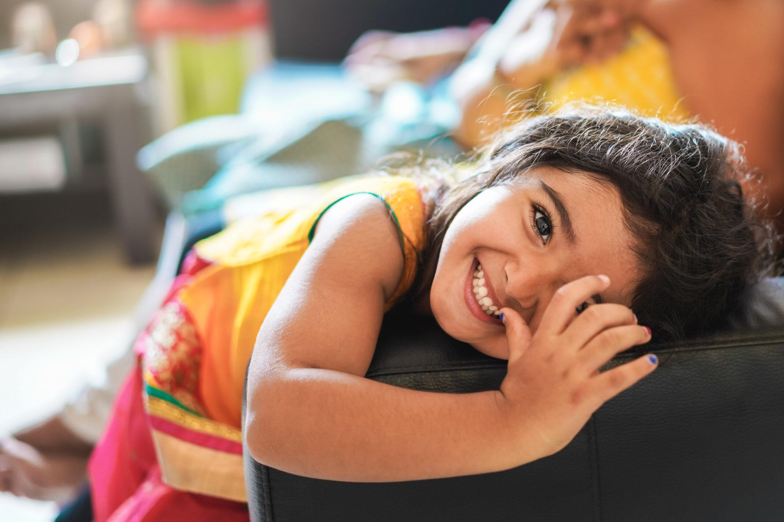 Happy indian child having fun sitting on sofa with parents at ho
